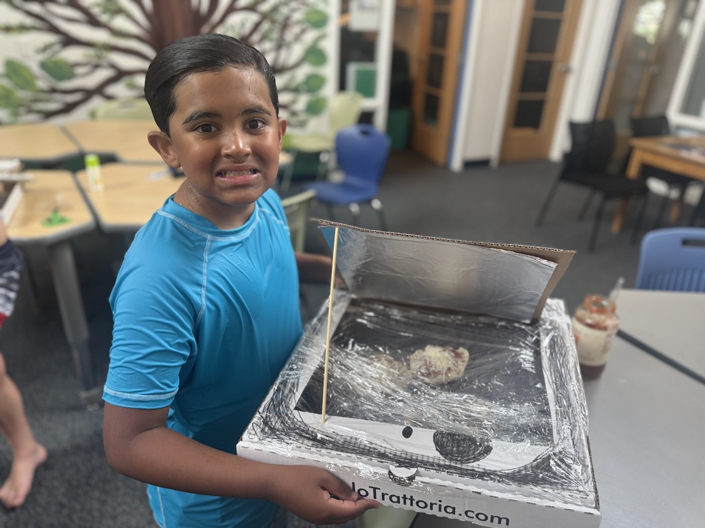 A boy wearing a blue shirt holds a box with a lid over a tray of food.