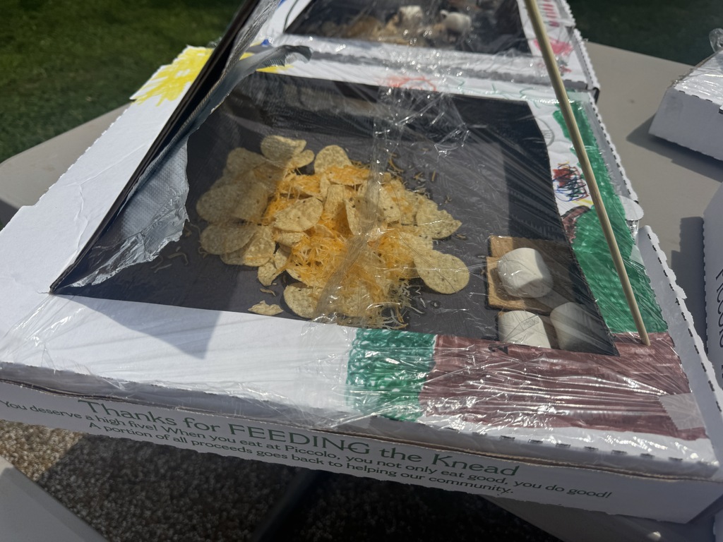 Pizza box with a transparent cover, filled with popcorn and marshmallows. Text reads "Thanks for feeding the bread." Background is blurry.