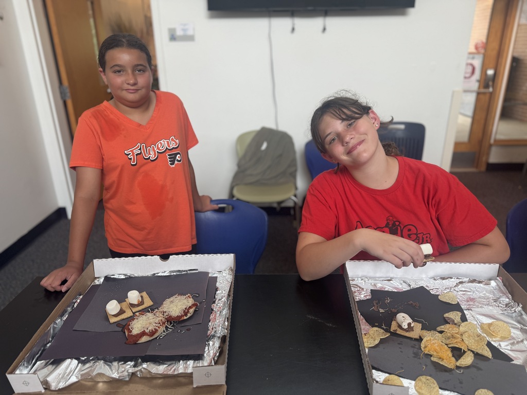 Two people in orange T-shirts sitting at a table with boxes containing food on top.