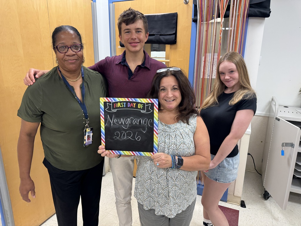 Four people stand in a room, holding a chalkboard. One woman holds a sign reading "Ms. Grossman 2026."