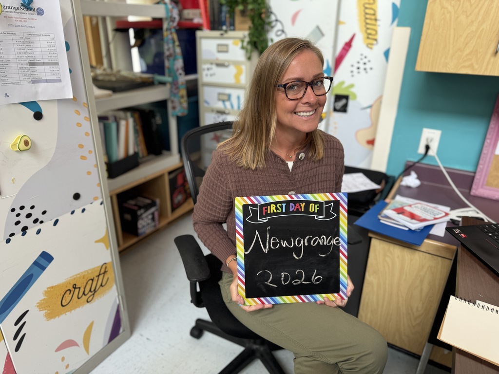 A woman sits in an office chair holding a blackboard that reads "First Day of 2026 Newgroups."
