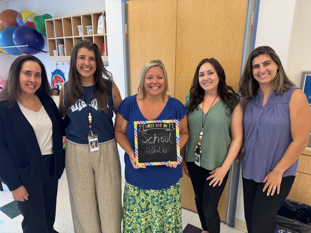 Five women stand in a room, one holding a chalkboard with "School 2020" written in rainbow colors.