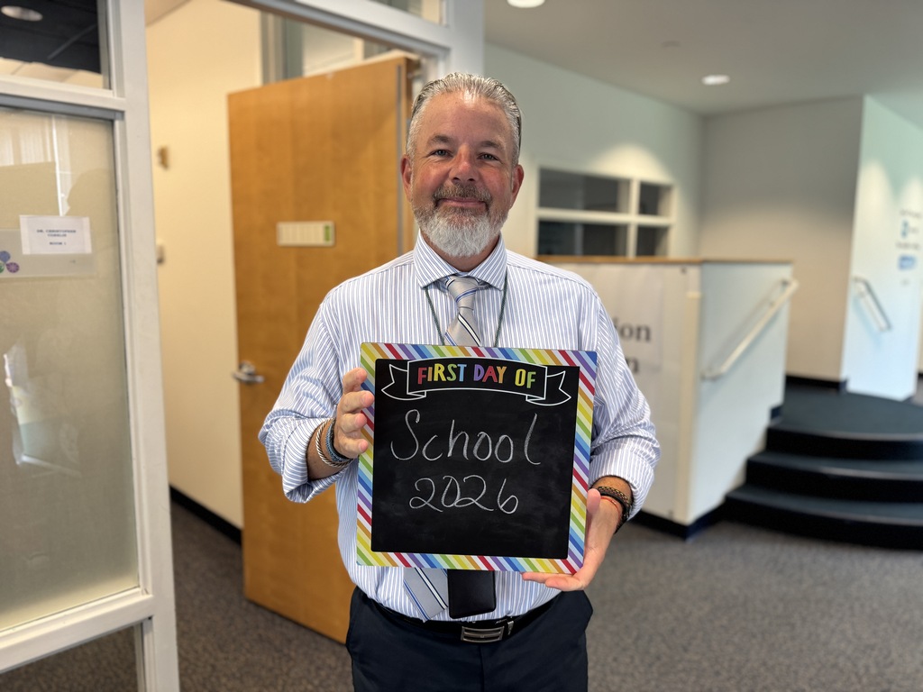 A man holding a blackboard that says "First Day of School 2026" in front of a door.
