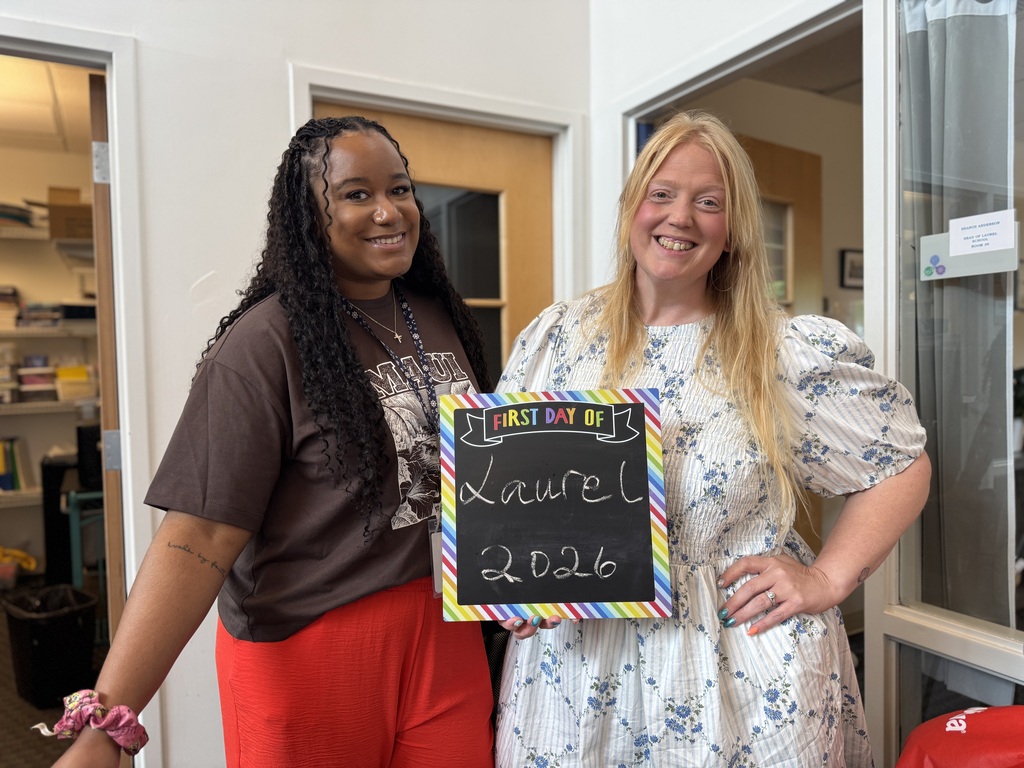 Two women pose with a chalkboard reading "Last Day of School, Laurel 2026" in a hallway.