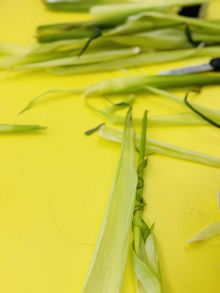 Several green plant stems, cut and tied together, are on a bright yellow surface. A knife with a black handle is nearby.