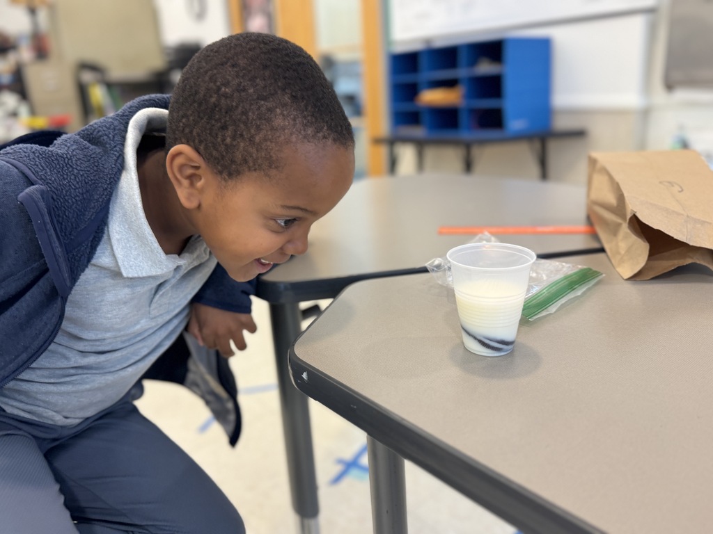 A child is looking down at a table with a cup of milk on it.