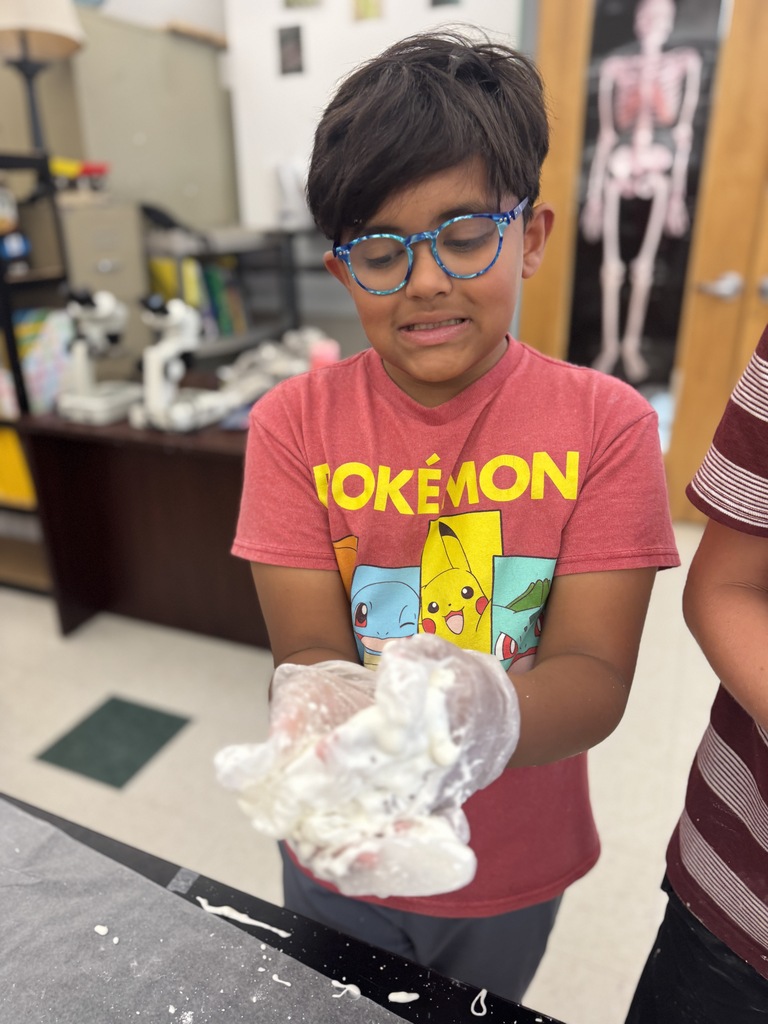 A young boy in a red shirt holds a plastic bag of white substance. A skeleton model and another person are in the background.