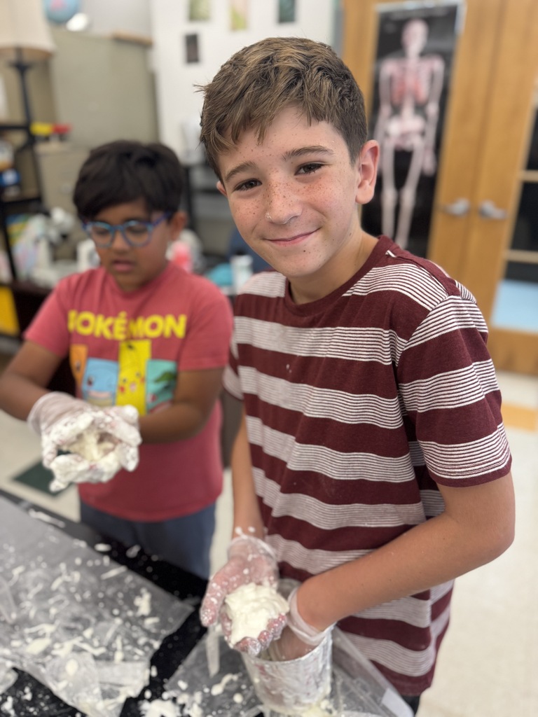 Two kids, one in red and one in striped shirt, are making dough on a table.