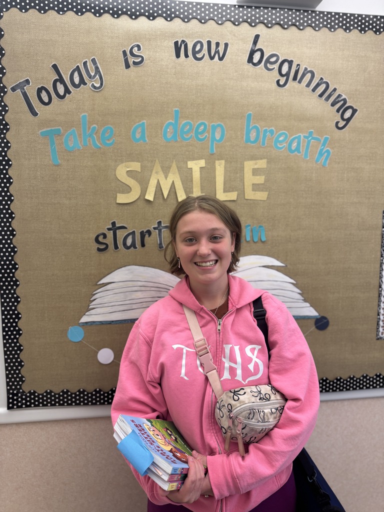 Woman in pink hoodie holds books in front of motivational poster that says, "Today is a new beginning."