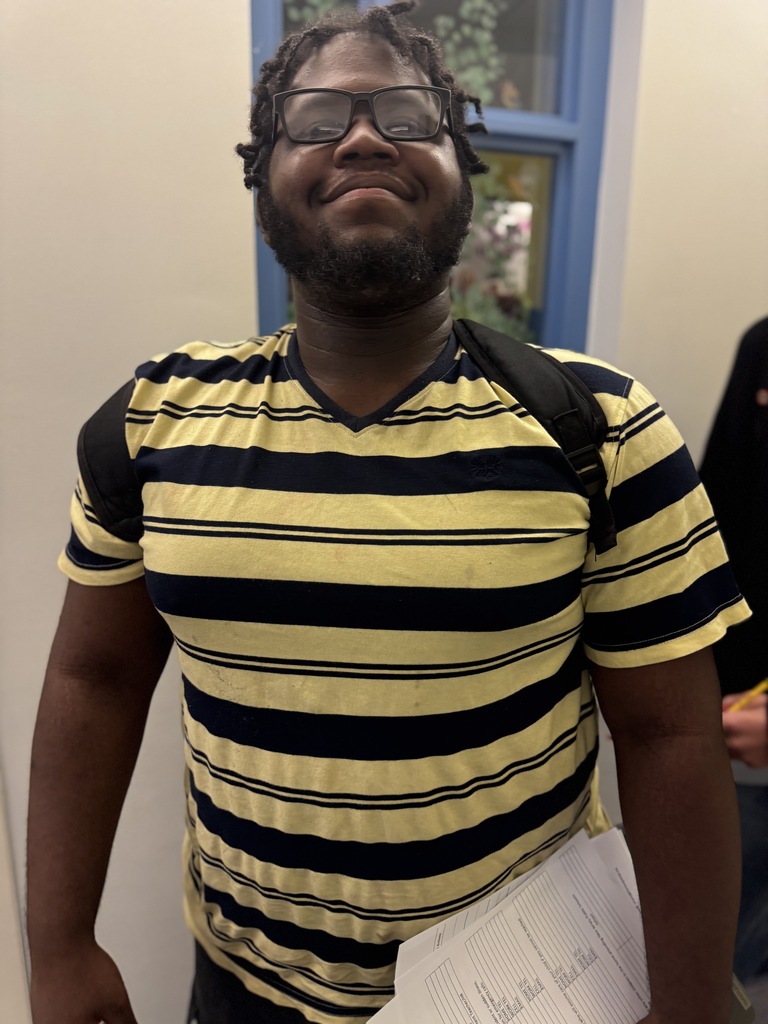 A man with a beard wearing glasses and a yellow and black striped shirt holds a piece of paper.