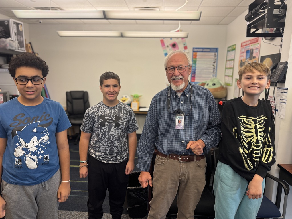 Four individuals in a room. Three young males and an older male. Two wear glasses.
