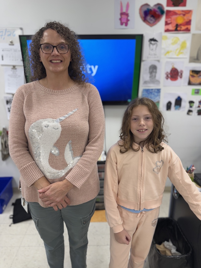 A woman and a girl stand next to each other. The woman has a unicorn sweater. A TV and decorations are behind them.