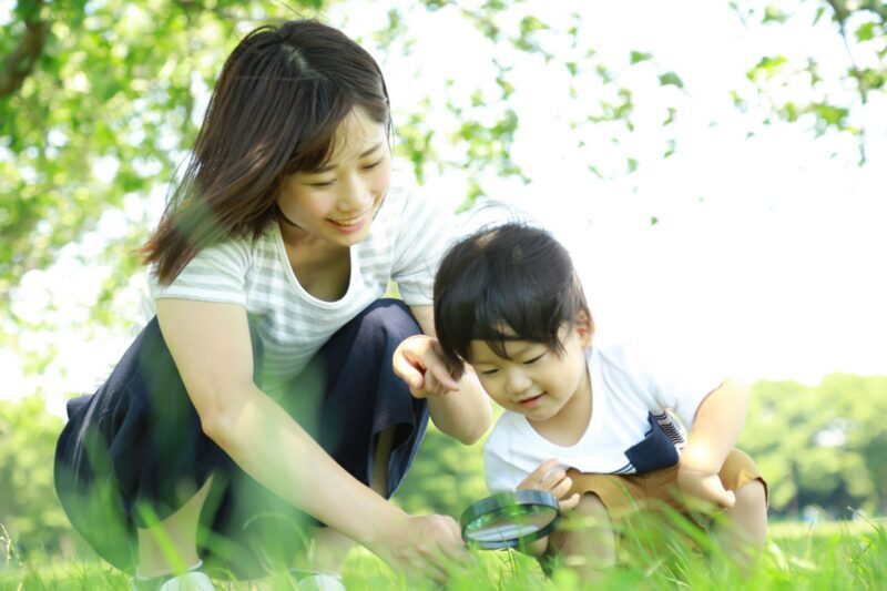 A mother and child playing in grass with a magnifying glass