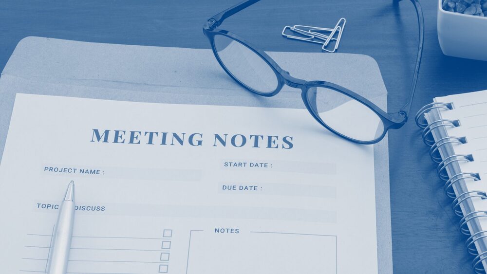 Meeting notes form on a desk with a pen, eyeglasses, and notebook