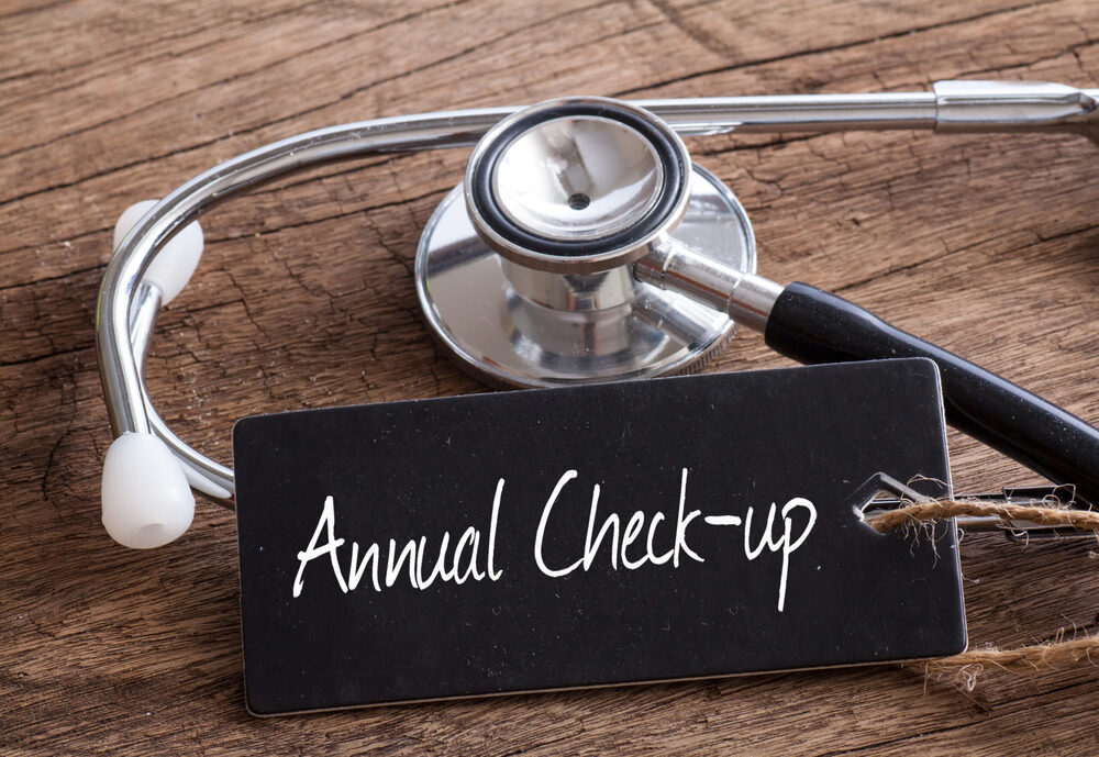 A stethoscope on a rustic wooden surface with a black tag reading 'Annual Check-up'.