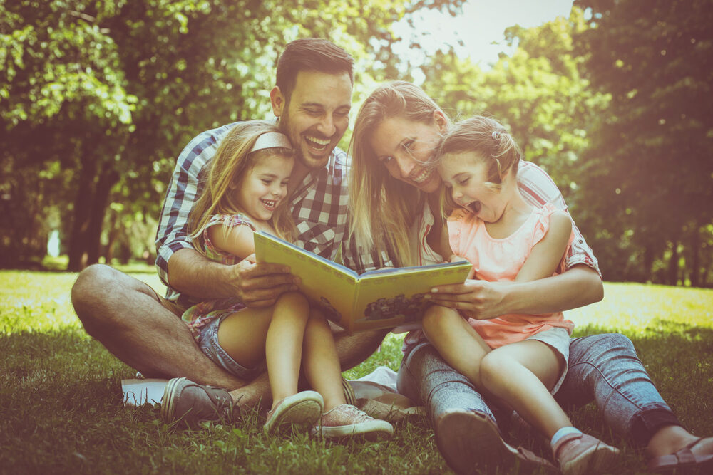 family sitting on the grass reading a book