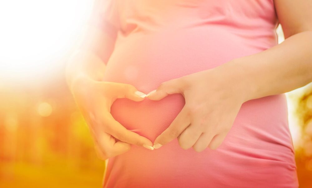 pregnant woman doing a hand heart over her stomach