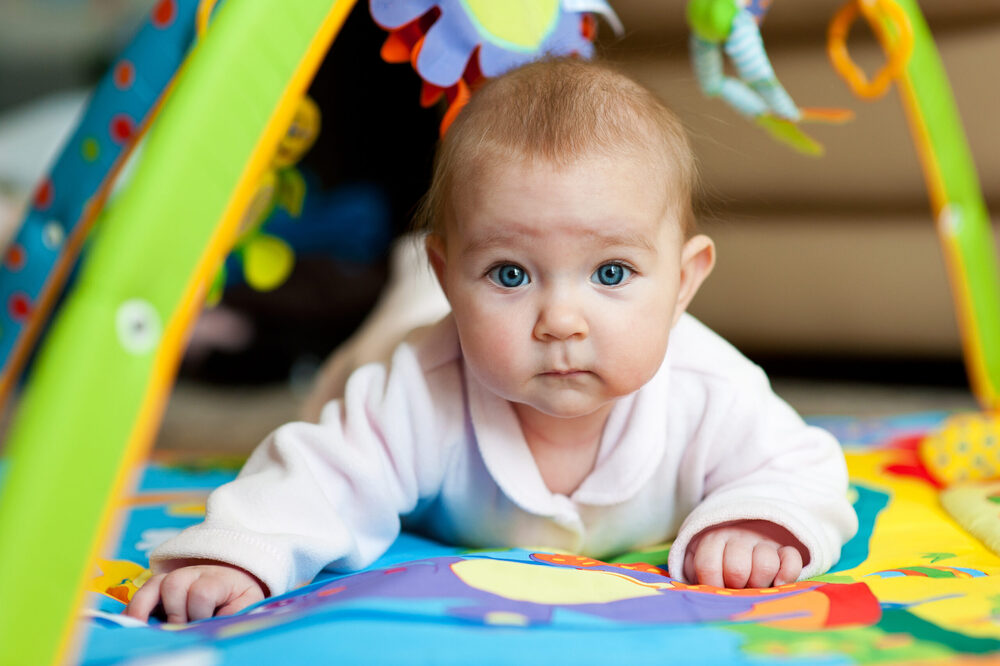 Baby with big blue eyes looking at the camera in a playmat