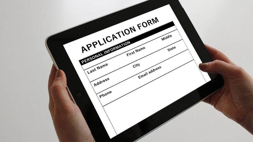 Person holding a tablet displaying an online application form.