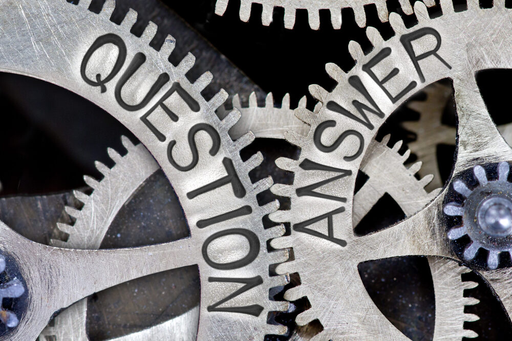 Close-up of interlocking metal gears engraved with the words 'QUESTION' and 'ANSWER'