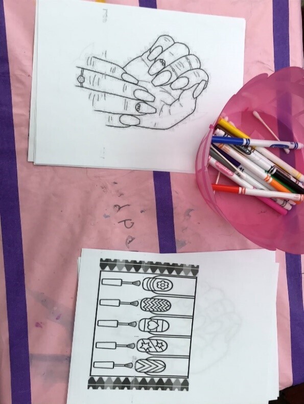 A table set up for a nail art coloring activity featuring printed line-art worksheets and a pink bowl of colorful markers