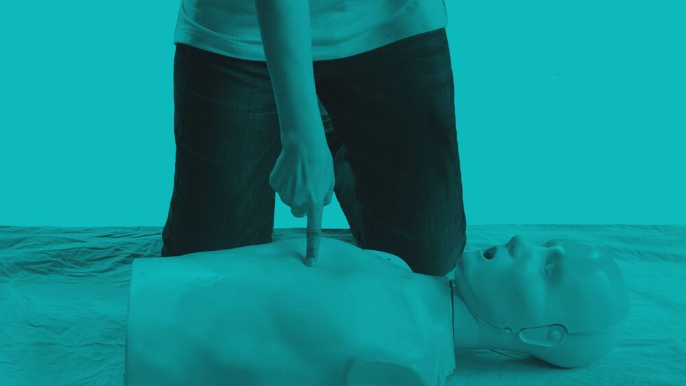 A person points to the center of an adult mannequin torso during CPR training, styled with a monochromatic teal overlay.