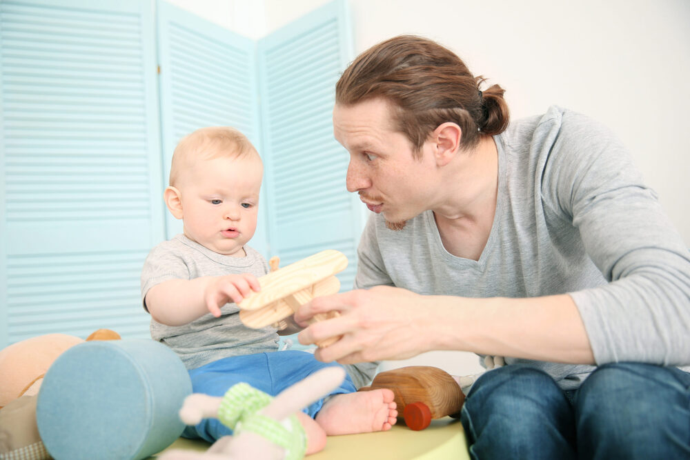 A dad playing with a wooden toy airplane with his baby.