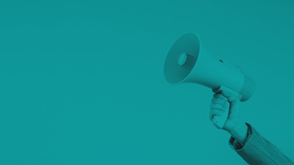 A hand holds up a megaphone against a solid background, styled with a monochromatic teal color overlay.