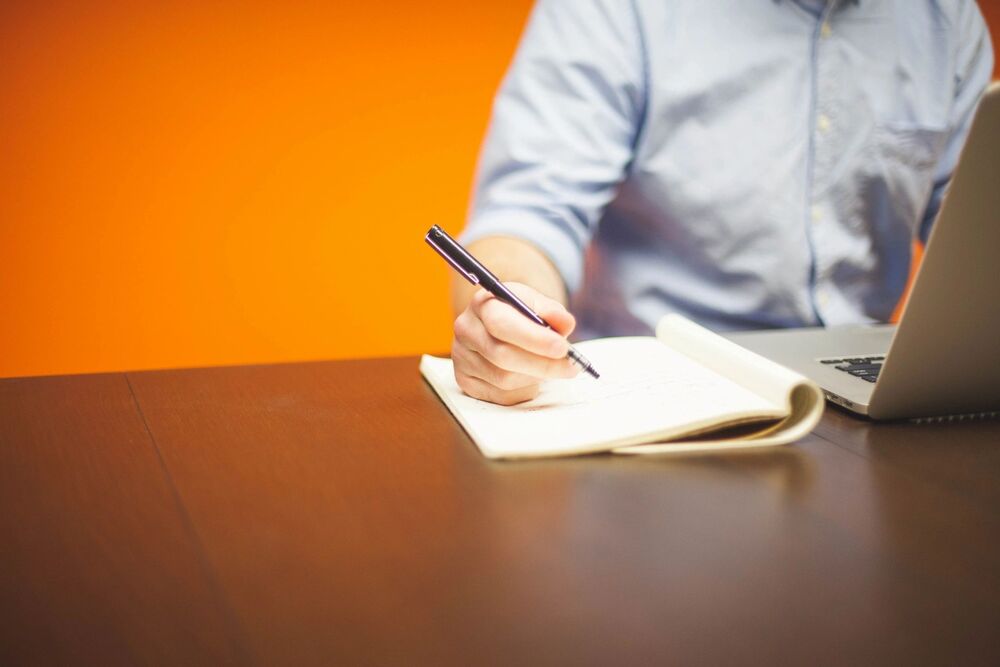 person using a computer and writing in a notebook