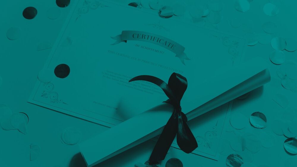 Rolled certificate tied with a ribbon on top of an achievement certificate and scattered confetti.