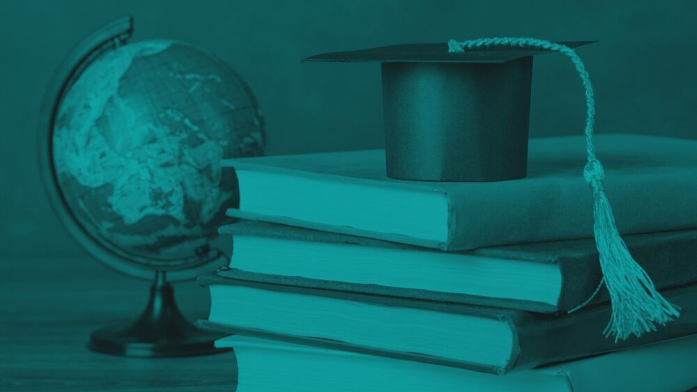 A miniature graduation cap sits on top of a stack of books next to a globe, styled with a monochromatic teal color overlay.