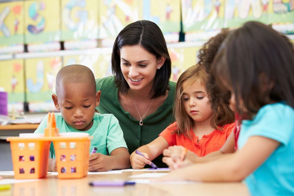 kids drawing in classroom with teacher watching