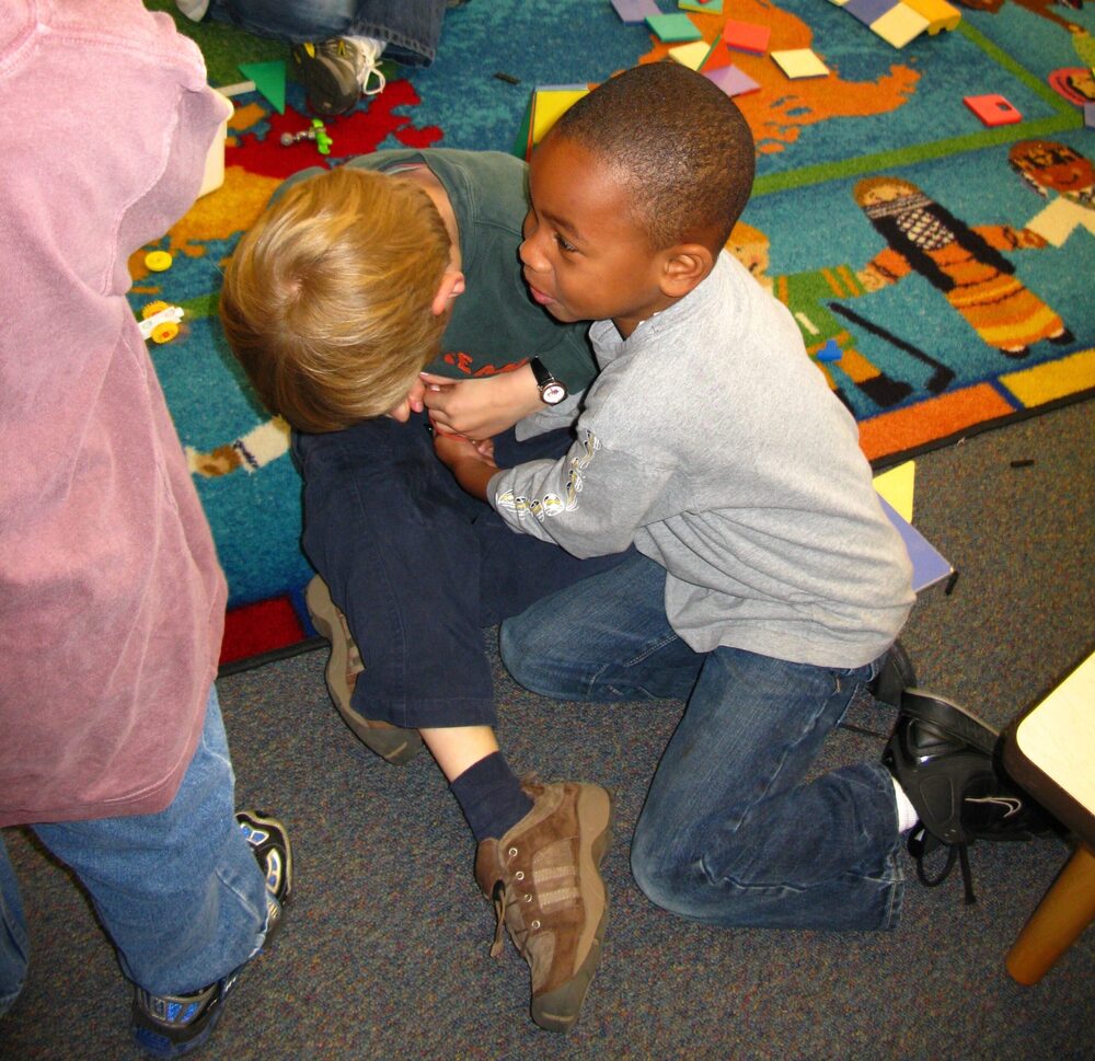 Two young boys on a play rug struggling over a small toy held between them.