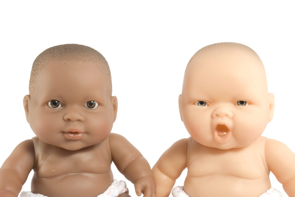 Two babydolls look at the camera, one black and one white.