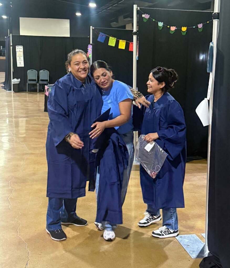 Three students getting ready for graduation hugging and crying tears of joy.