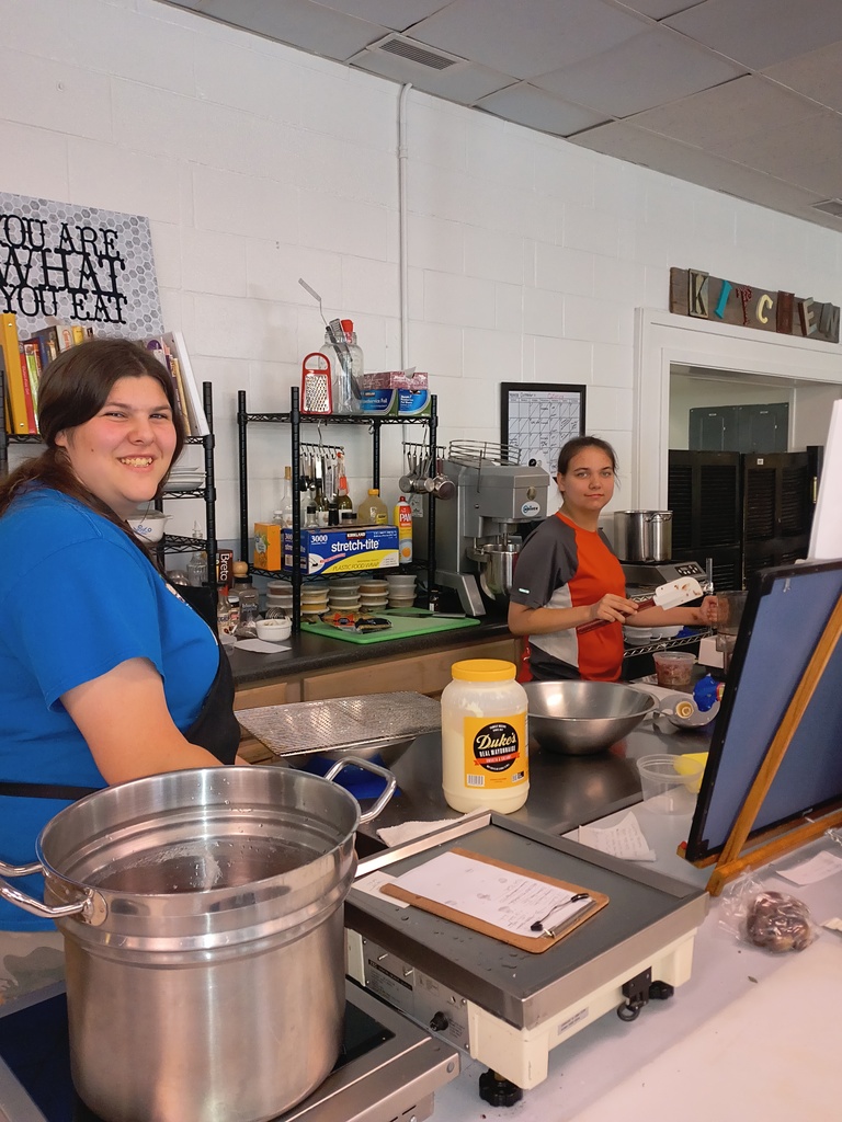 two female students pausing their work in a kitchen to smile for the camera