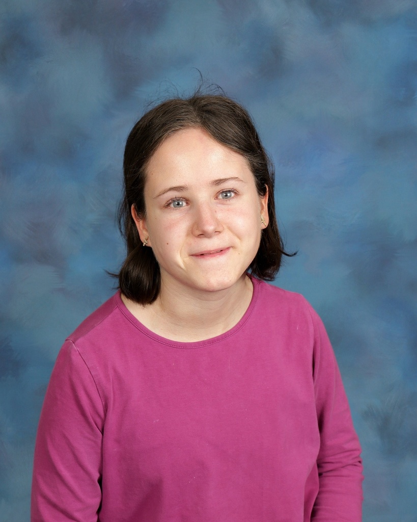 photo of Charlotte in front of a blue background. she is wearing a bright pink shirt