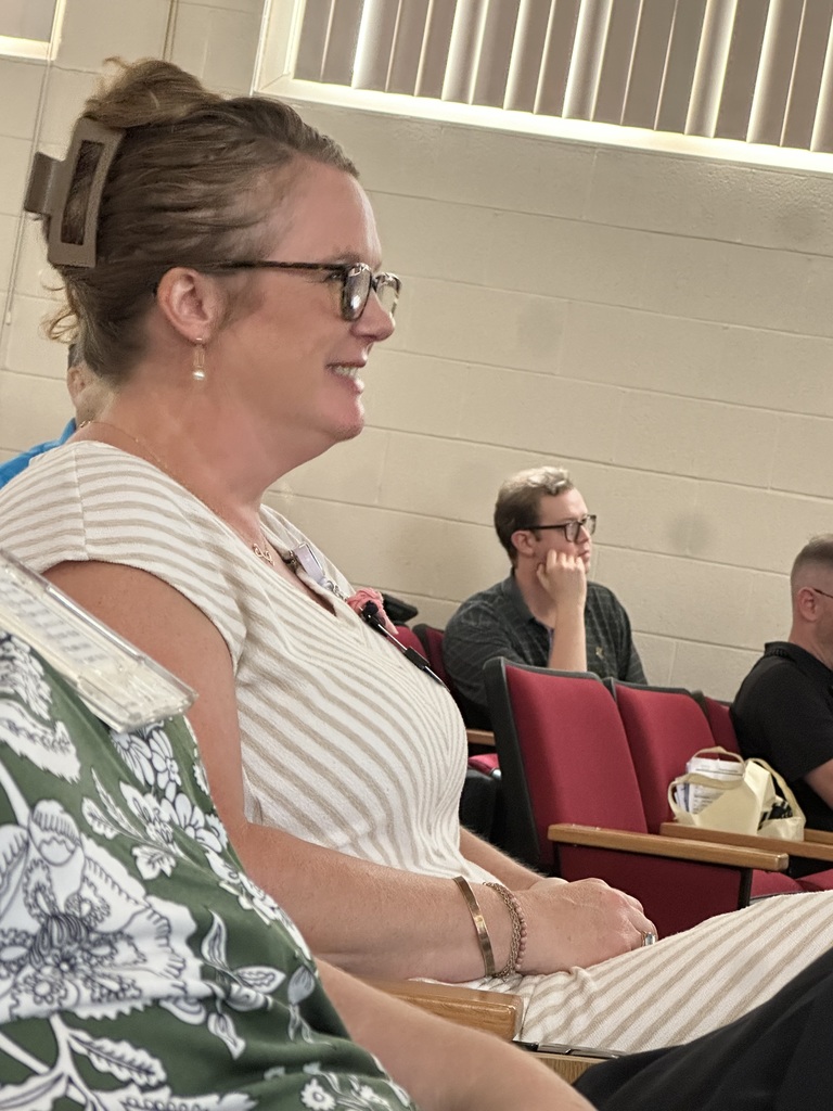 one female staff watching the current presenter on stage. she smiles as she is engaged in the session