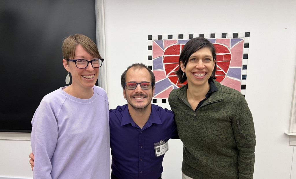 Lindsay on the left, Neil in the middle, and Heather on the right smiling together in front of a heart- themed artwrork.