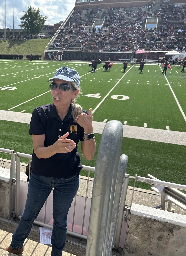 Thelma Schoreder is signing to the audience with the football field spanning out behind her with the marching band playing in the background.