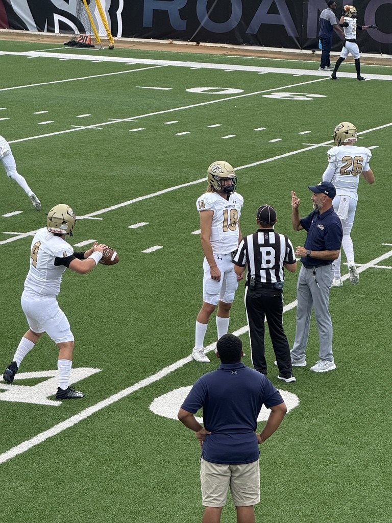 Gallaudet's head coach is seen signing to player #18 on the football field.
