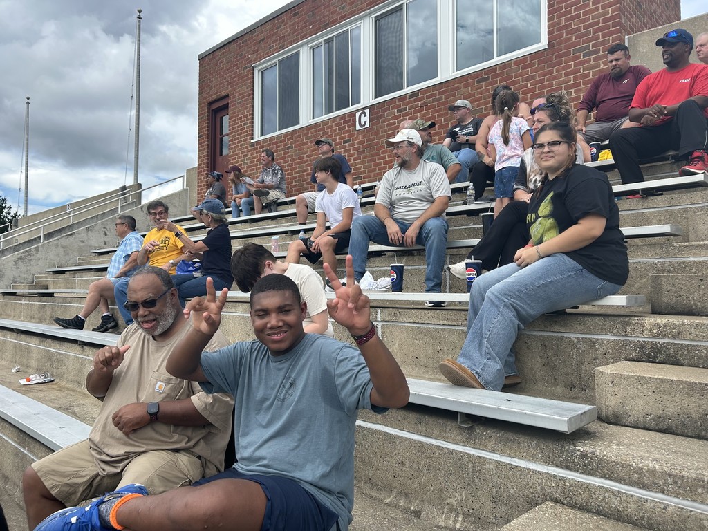 Fans are sitting and watching the game, a boy in the front is turned and giving peace signs to the camera.