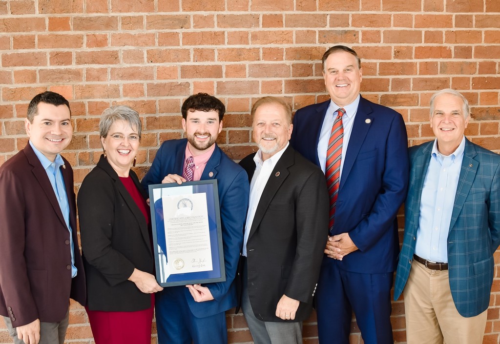 Left to Right: Delegate Phil M. Hernandez, Charity Reedy Warigon, Deputy Secretary of Education Zachary Jacobs, Senator Christopher T. Head, Delegate W. Chad Green and , Senator Mark D. Obenshain stand outside in front of a brick wall, while smiling and holding the proclamation between them.