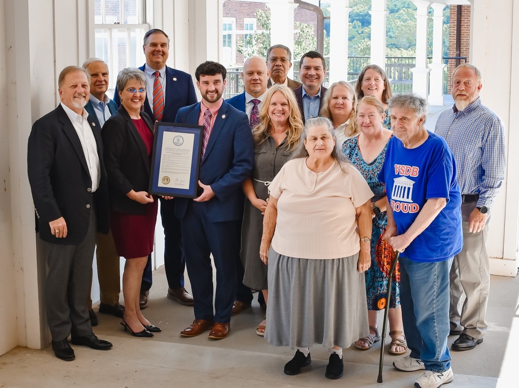 Senator Christopher T. Head, Senator Mark D. Obens Lanhain, Delegate Phil M. Hernandez, Delegate W. Chad Green, Sr., Scott Alleman, Carolyn Berry, JH Cline, Jr., Daphne Cox, Ronaldier, Vera Wilson, Christine Ogden, Dr Rhonda Jennings Arey and Ryan Whitworth stand in a group outside smiling at the camera. Charity Warigon and Deputy Secretary of Education Zachary Jacobs Zachary hold the proclamation.
