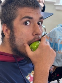 A male student is biting into a green apple and looking at the camera