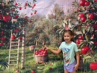 A student is in front of a apple field background and smiling while reaching for an "apple basket"
