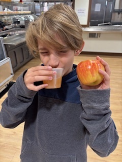 A student is drinking apple cider and holding a yellow and red apple