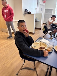 a student sits by a table while biting into a red apple
