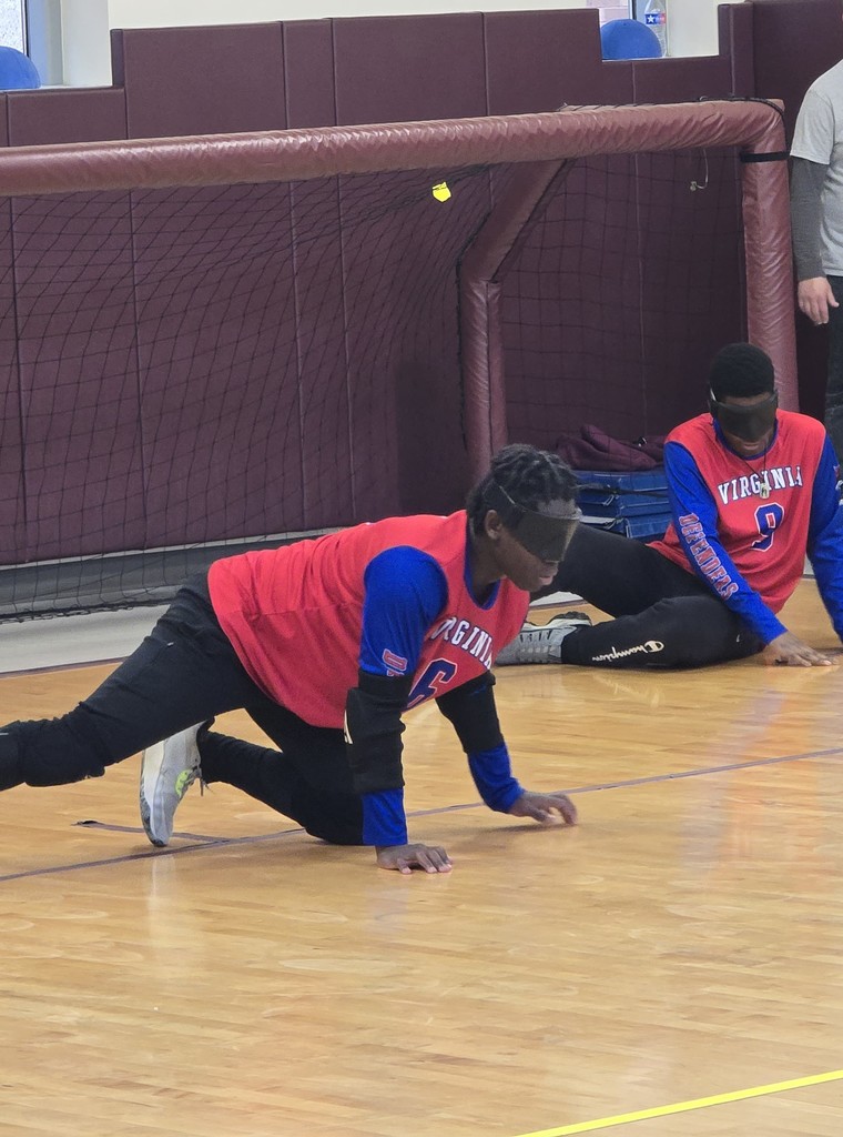 Two VSDB students are perched on the floor in front of a goal. The blind fold is over their eyes and they look ready to pay! 