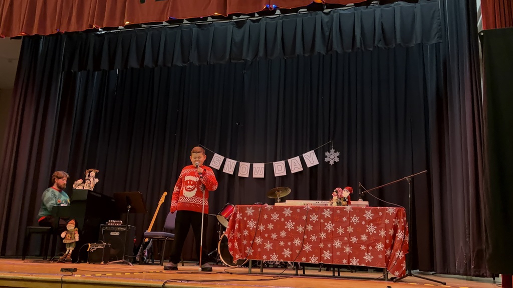 A student is on stage singing, accompanied by someone at the piano